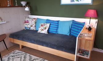 A stylish living room with a modern sofa and colorful cushions. A small lamp and a shelf complement the cozy atmosphere.