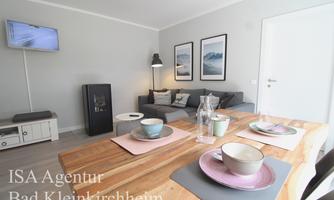 A modern living room with a cozy sofa and a dining area. The table is set, and decorative pictures hang on the wall.