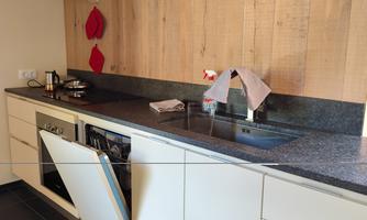 A modern kitchen with wood paneling and a large, dark countertop. The cabinets are light, and the kitchen equipment is visible.
