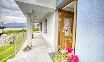An inviting entrance area of a house with a wooden and glass door. Colorful flowers stand beside the entrance and provide a beautiful contrast to the modern architecture.