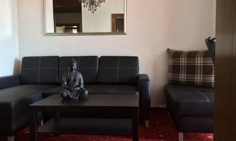 A modern living room with a black couch and a small table. On the table sits a Buddha statue and in the background hangs a mirror.