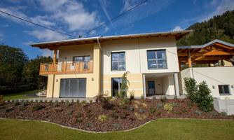 A modern house with a balcony and large windows. The garden is well-maintained and designed with colorful flowers.
