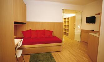 A modernly furnished room with a red sofa and wooden shelves. There is a small table and a television on the wall.
