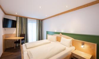 A modern hotel room with two single beds and a television. The room has large windows and a cozy atmosphere.