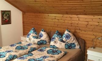 A cozy bedroom with two beds and colorful bedcovers. The wooden walls give the room a warm atmosphere.