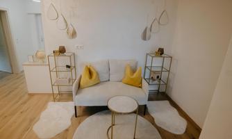 A modern living room with a bright sofa and yellow cushions. Next to the sofa are elegant shelves and a round table on a soft carpet.