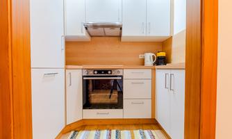 A modern kitchen with white cabinets and a stove. A colorful rug lies on the floor.