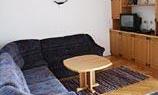 A cozy living room with a blue sofa and a table. In the background, there is a TV on a wooden shelf.