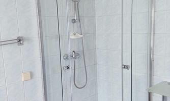 A modern shower cabin with glass walls and a showerhead. The walls are brightly tiled and the cabin is integrated into a clean bathroom.