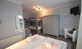 A cozy room with a double bed and a bunk bed. There is a wardrobe, a television, and a seating area.