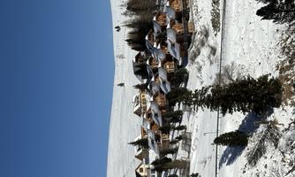 A picturesque winter village with snowy hills and beautiful wooden houses. The sky is clear and blue.