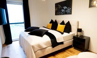 A modern bedroom with a comfortable bed and elegant pillows in black and yellow. The large window front lets in plenty of daylight and offers a view outside.