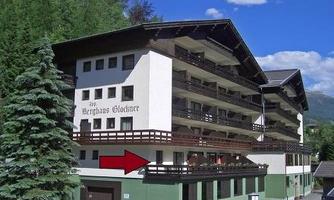 A modern building with several floors and balconies. It is surrounded by trees and has a blue sky in the background.