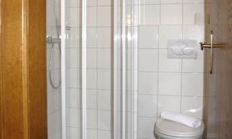 A small bathroom with a shower and a toilet. The walls are tiled and the floor has a dark design.