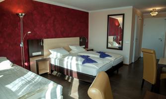 A modern bedroom with a double bed and a cozy chair. The walls are red, and there is a mirror as well as a table.