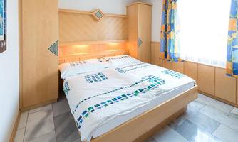 A cozy bedroom with a double bed and light wooden interiors. The windows are decorated with colorful curtains and let in plenty of light.
