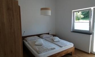 A modern bedroom with a large double bed and wooden furniture. The room has a window with a view and a simple, inviting style.