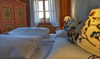 A cozy bedroom with two beds and decorative pillows. The window offers a beautiful view outside and the walls are painted in warm tones.