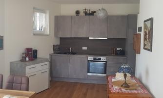 A modern kitchen with gray cabinets and a stove. The floor is made of wood and there is a small dining table.