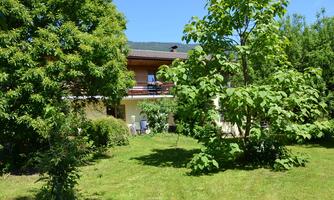 A beautiful garden with lush greenery and trees. In the background, a cozy house with balconies is visible.