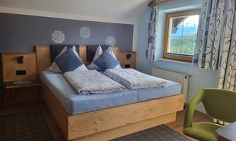 A cozy bedroom with a double bed and blue pillows. The room has a window with a view of the mountains and stylish decoration.