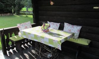 A cozy table on a terrace with a colorful tablecloth and decorative cushions. In the background, there is a garden with fresh grass.