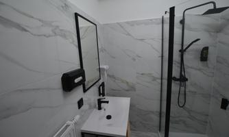 A modern bathroom with marbleized walls and an elegant shower. There is a wash area with a black faucet and a mirror.