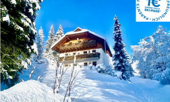 A charming chalet in a winter landscape, surrounded by snow-covered trees. The clear blue sky gives the scene a tranquil atmosphere.