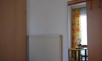 A simple room with a radiator and a door. In the mirror, a table with a bouquet of flowers and a curtain can be seen.