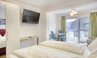 A modern room with two beds, a television, and a balcony. The space is bright and inviting, with a view of the surrounding landscape.