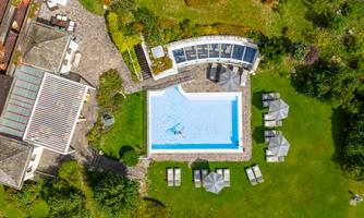 A beautiful outdoor pool surrounded by a well-maintained lawn and loungers. The view shows a green landscape with trees and bushes.