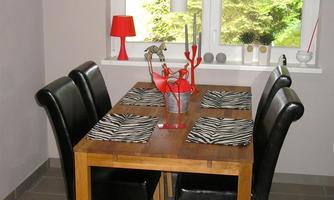 An elegant dining area with a wooden table and black chairs. On the table, there are striped placemats and decorative elements in red.