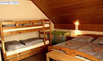 A cozy bedroom with a bunk bed and a double bed. The walls are made of wood and there is warm light.