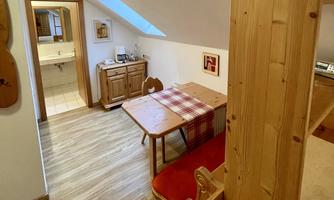 A cozy room with wooden furniture and a table. The sloping roof and warm light create an inviting atmosphere.