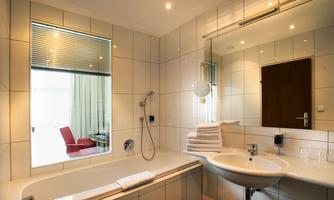 A modern bathroom with a bathtub, sink, and large mirror. A red chair is visible in the background through the window.