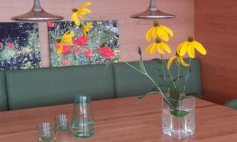 A table with yellow flowers in a glass vase stands in a modern room. In the background, there are pictures with colorful flower motifs.