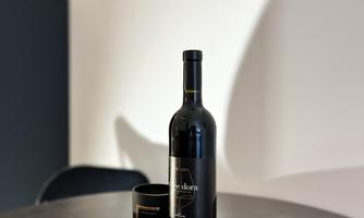 A wine bottle is standing on a round black tray. Next to it is a black glass.