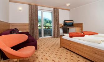 A cozy hotel room with a double bed and a modern armchair. Large windows offer a view of the mountains.