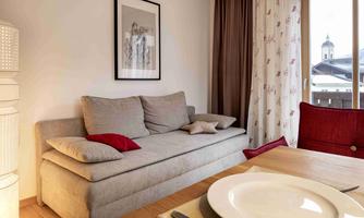 A modern living room with a beige sofa and a dining table. A cozy space with wooden flooring and large windows.
