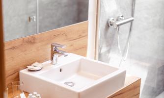 A modern bathroom with an elegant sink on a wooden shelf. In the background, a shower is visible, showcasing a minimalist style.