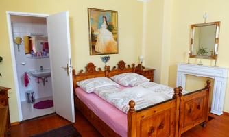 A cozy bedroom with a double bed and a beautiful painting on the wall. In the background, a bathroom is visible, accessible through an open door.