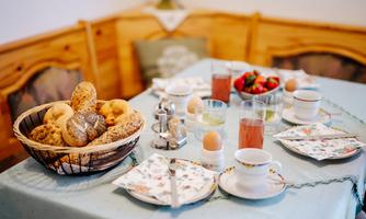A laid breakfast table with rolls, boiled eggs, and fresh strawberries. Drinks in glasses and cups complete the breakfast.