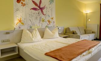 A cozy bedroom with a large bed and a comfortable couch. The walls are designed in soft colors, with a floral motif above the bed.