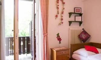 A cozy room with a single bed and a small table. The balcony door opens to a beautiful view with a rustic railing.