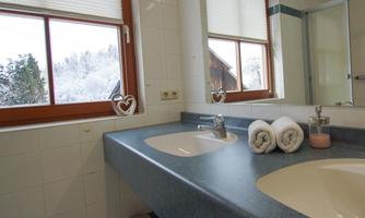 A bright bathroom with a double sink and large windows. In the background, a snowy landscape can be seen.