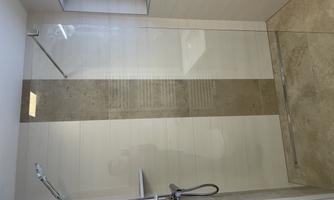 Modern shower with clear glass walls and gray tiles. Large window provides plenty of daylight.