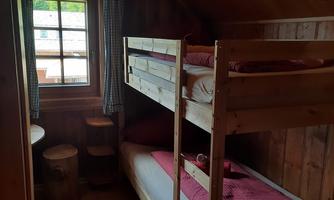 A cozy bedroom with two wooden bunk beds. The room has wooden walls, a window, and a small table.
