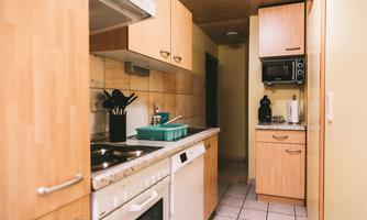 A modern kitchen with wooden cabinets and a clear workspace. The room is bright and well-organized, with appliances and cooking utensils.