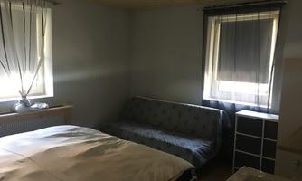 A simple bedroom with a bed and a sofa.  
Windows with bright curtains let light in.