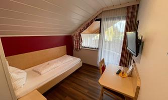A cozy room with a single bed, desk, and television.  
Large windows provide plenty of natural light and a pleasant atmosphere.